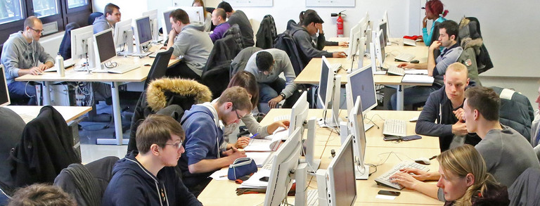 Mehrere Studierende sitzen in einem Raum mit mehreren Computern